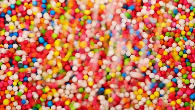Multi-colored candies drop into clear cups.