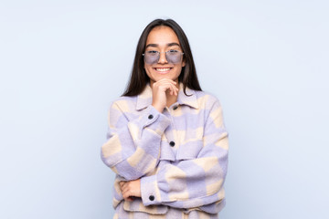 Young Indian woman isolated on blue background with glasses and smiling