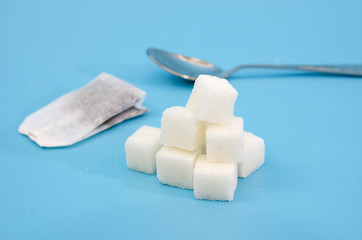 white sugar cubes, tea bag and spoon on a blue background.