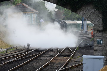 A U class locomotive pulling  a steam train under a road bridge.
