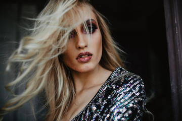 Serious woman with blonde hair looking to camera. Indoor shot of glamorous caucasian girl with bright makeup.