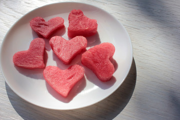 Fototapeta na wymiar Watermelon slices in the heart shape on a white plate on wooden table. Top view, copy space. 