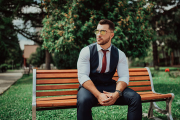 Fototapeta premium a young sexy businessman in a suit sitting in park on job break