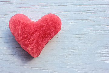 Obraz na płótnie Canvas Red heart on wooden table. Heart-shaped slice of watermelon on white background. Top view, copy space