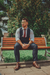 Obraz premium a young sexy businessman in a suit sitting in park on job break