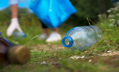 Volunteer collecting bottles in the forest. Environment pollution concept.