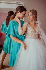 stylish happy bride dressing in dress, smiling to bridesmaids, at window, rustic wedding morning preparation. bridal getting ready. emotional moment. space for text. black white photo