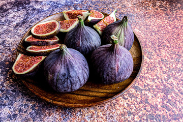 Whole figs and one fig sliced in half on top of a teak garden table. Focus is on the sliced fig. Fresh, all, half and quarter figs in a plate. Copy space.