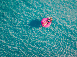 Young relaxed woman in a swimsuit swims in the water on an inflatable flamingo and sunbathes. View from above.