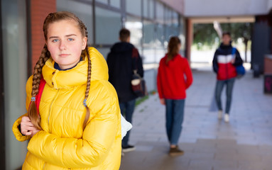 Portrait of female teenage student with braids in warm yellow puffer jacket on her way to college...