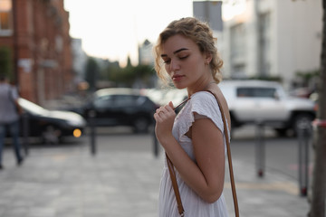 Beautiful woman in white dress posing at city street