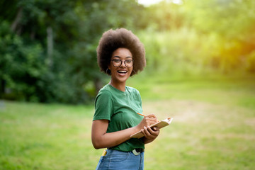 Positive Black Student Girl In Eyeglasses Standing Outdoors Taking Notes To Notepad