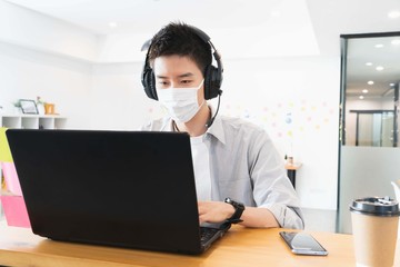 Young smart asian business man in casual shirt at the office wearing medical face mask under the outbreak of the virus,