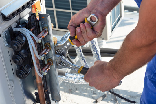 HVAC technician is working on air conditioner units on a roof of new industrial building.Technician hand using fix wrench to tighten outdoor unit of air condition. Man holds a wrench in his hand.
