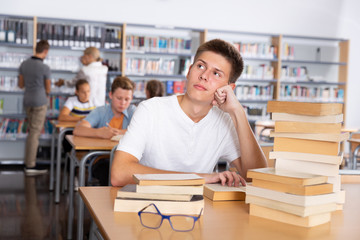 Schoolboy sitting with stacks of books in school library indoor