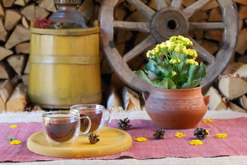 A couple glass mugs of black tea on the background of wooden wheel, yellow tub and stack of firewood.