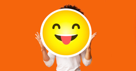 Black bushy man holding happy cheeky emoji emoticon in front of head