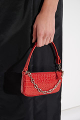 Beautiful red leather handbag in girl's hand. Luxury handmade bag against black dress with reptile...