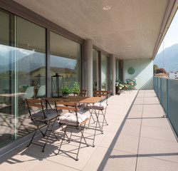Modern house terrace with wooden table and chairs. A seedling, a bottle and a lantern on the table