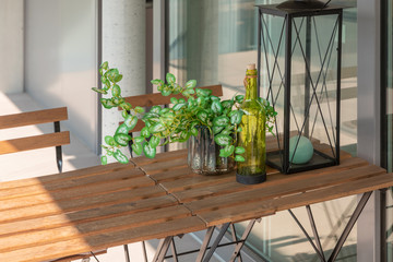 Modern house terrace with wooden table and chairs. A seedling, a bottle and a lantern on the table