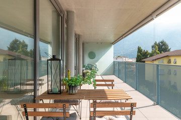 Modern house terrace with wooden table and chairs. A seedling, a bottle and a lantern on the table