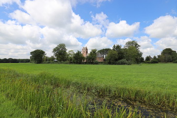 Fototapeta na wymiar Beautiful panoramic view of a characteristic Dutch church in the green meadows and surrounded by trees.