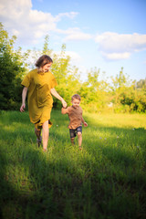 Cute baby boy and mother walking hand in hand on green lawn. Summertime photography for ad or blog about motherhood