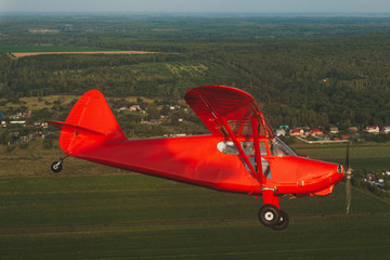 Vintage red small plane Stinson in flight over the green forest.