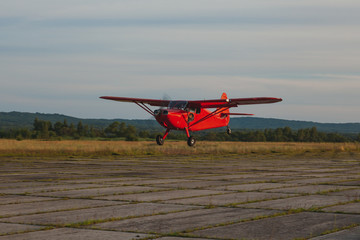 A vintage red Stinson small plane flies low over a private concrete runway.