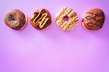 Group of chocolate donuts with different icing on top of them, isolated on purple background. Negative space available.