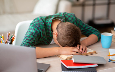 Tired school boy sleeping at desk while doing homework