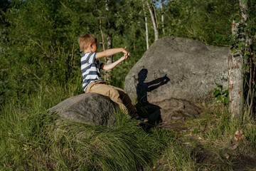 Caucasian boy in a striped tee shirt playing shadow theatre on a big rock doing a crocodile jaws with his hands © Yulia Raneva