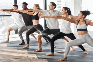 Fototapeta na wymiar Group of multicultural yogi making warrior pose in modern studio, training together