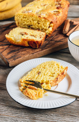 Loaf of banana bread on a wooden cutting board with cup of tea on rustic wooden table.