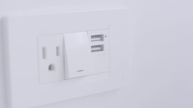 On the wall of a white room a device allows you to charge your devices on its usb ports, turn the light on or off and plug in three legged cables.