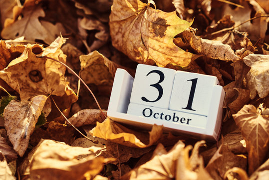 Wooden calendar block with date 31 october on a falling autumn leaves background
