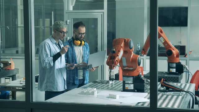 Two men control robotic machines in laboratory, checking them.