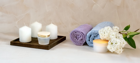 Cosmetic mockup - lilac flower, towels, aromatic candles, face cream containers best suited for relaxing and skin care