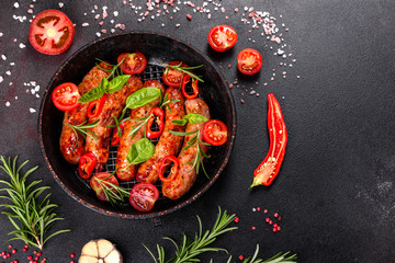 Grilled sausages with vegetables and spices on black background