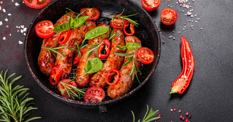Grilled sausages with vegetables and spices on black background