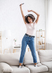 Dancing with headphones and relax at home. Happy woman with smartphone on sofa in living room