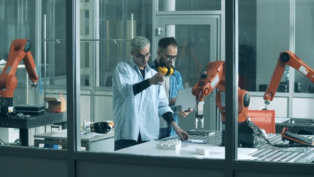 People work with automated arm at a factory. Innovation, hi-tech education, science studying concept.