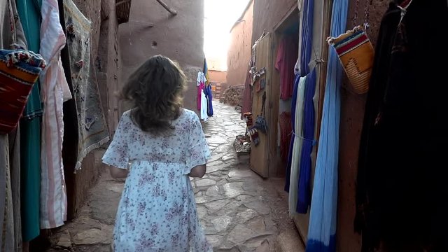 Unrecognizable woman walking through empty street of outdoor market stall in arabian ancient town Ait Benhaddou Morocco, slow motion