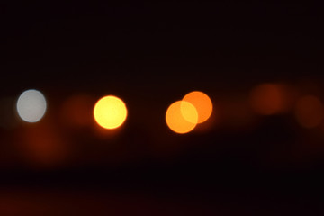 bokeh effect with out-of-focus lights against a dark background. The lights appear as soft, circular orbs in shades of orange, yellow, and a single white dot, creating a dreamy, abstract night scene.