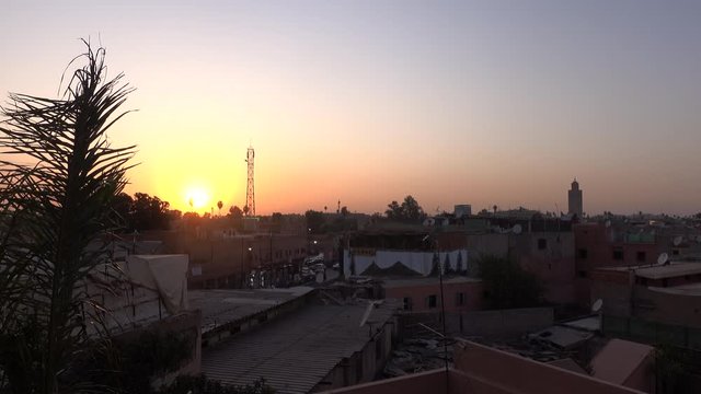  Stunning orange sunset sky over the Marrakech medina city and palm tree leaves moving with wind from viewpoint terrace during travel vacations in Morocco.