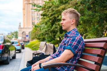 A young man sits on a bench in a Park against the background of old buildings in Moscow