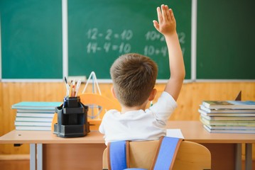 Back to school. A schoolboy is reading a book while sitting at the table for the first time at school on the background of the school blackboard.