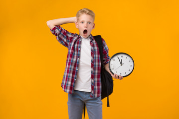 Surprised shocked little boy holding clock at studio