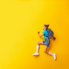 Fototapeta na wymiar Back to school! Cute hardworking schoolgirl Jogging on a yellow background.