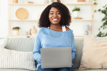 Black woman sitting on couch with pc looking at camera